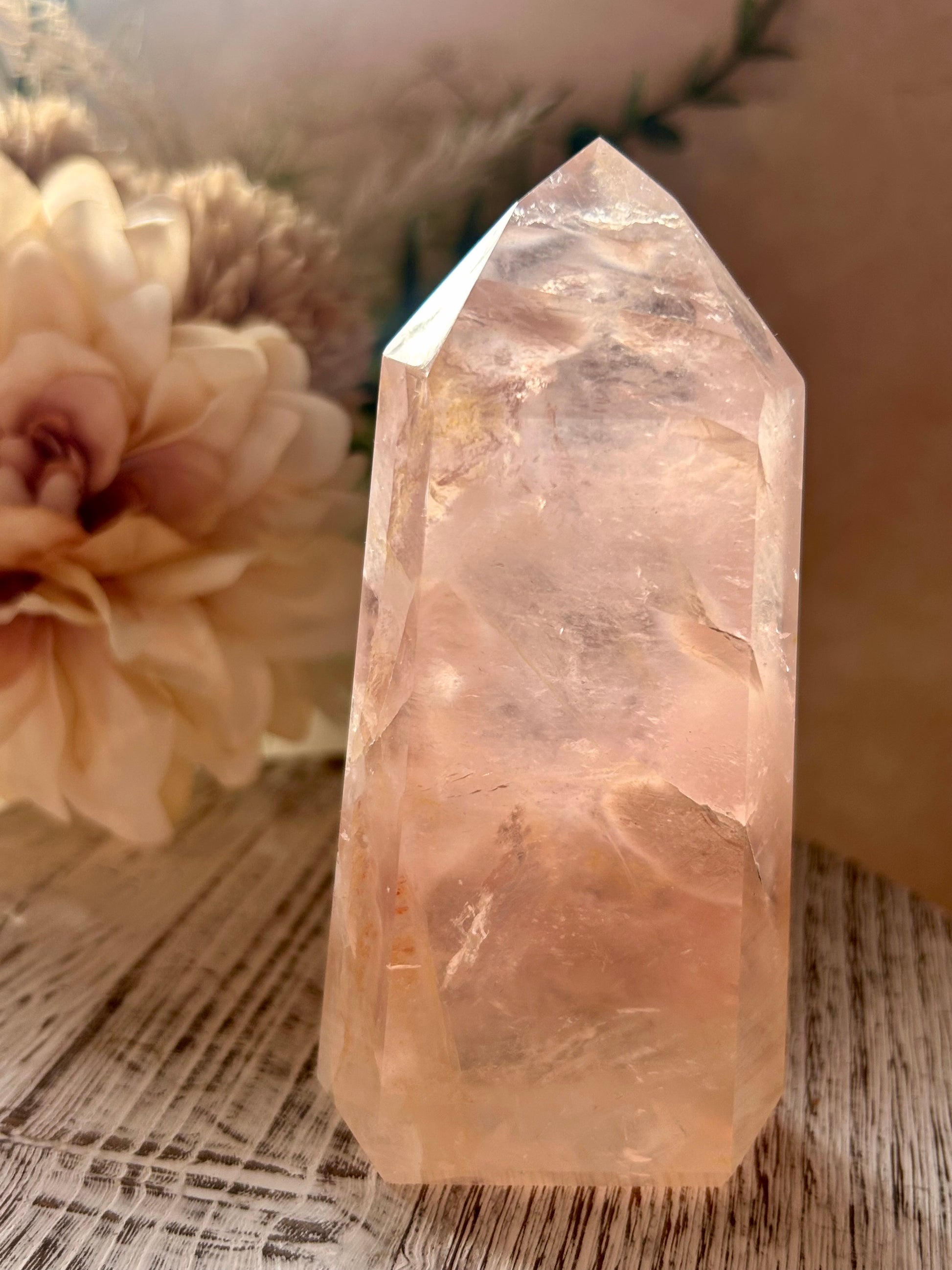 Pink Rose Quartz crystal on a wooden surface with flowers in the background.
