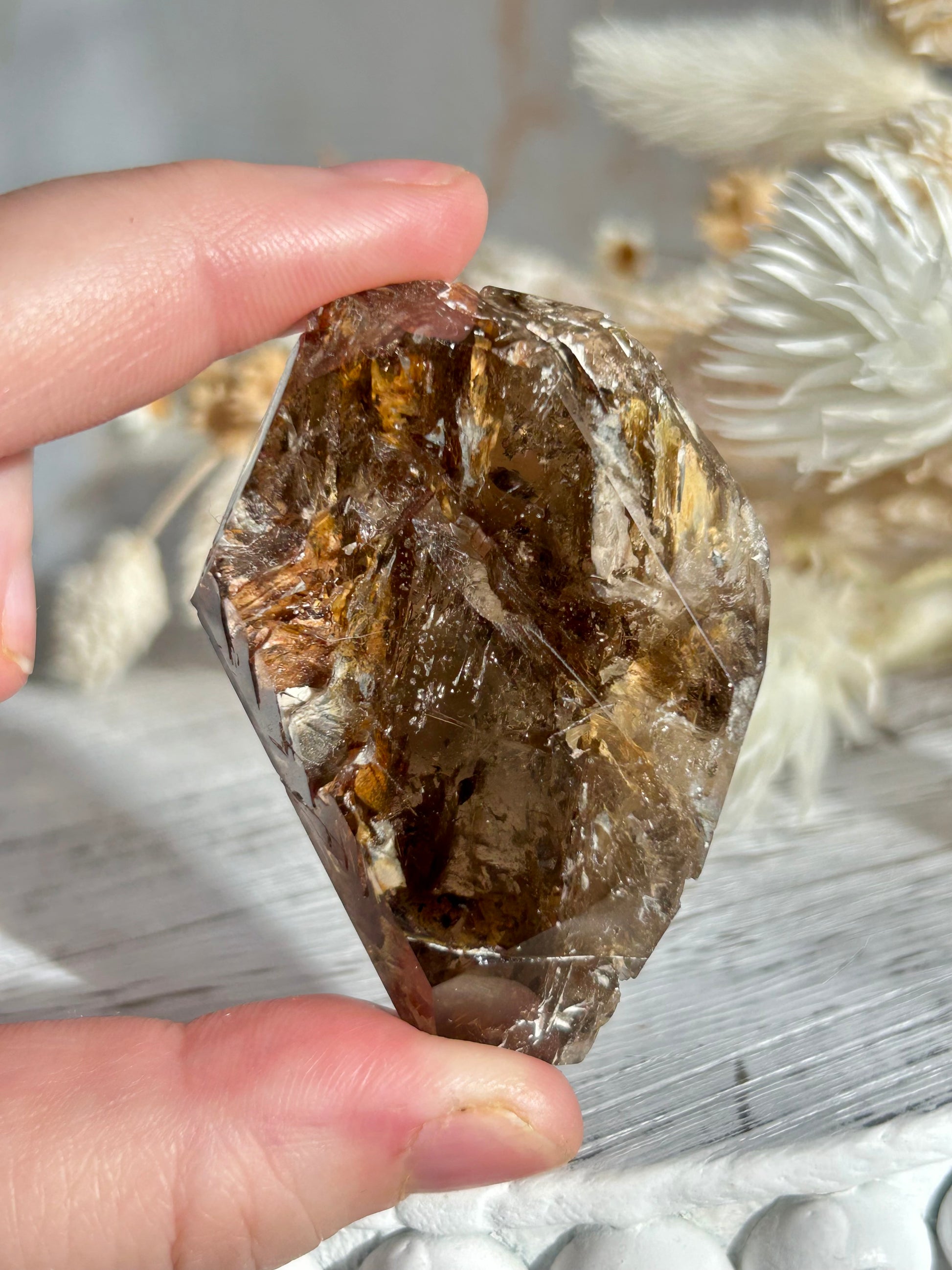 Golden Elestial Quartz crystal tower with visible layered terminations and internal inclusions, polished to a high shine. Photographed in warm natural light with soft cream dried florals in the background.