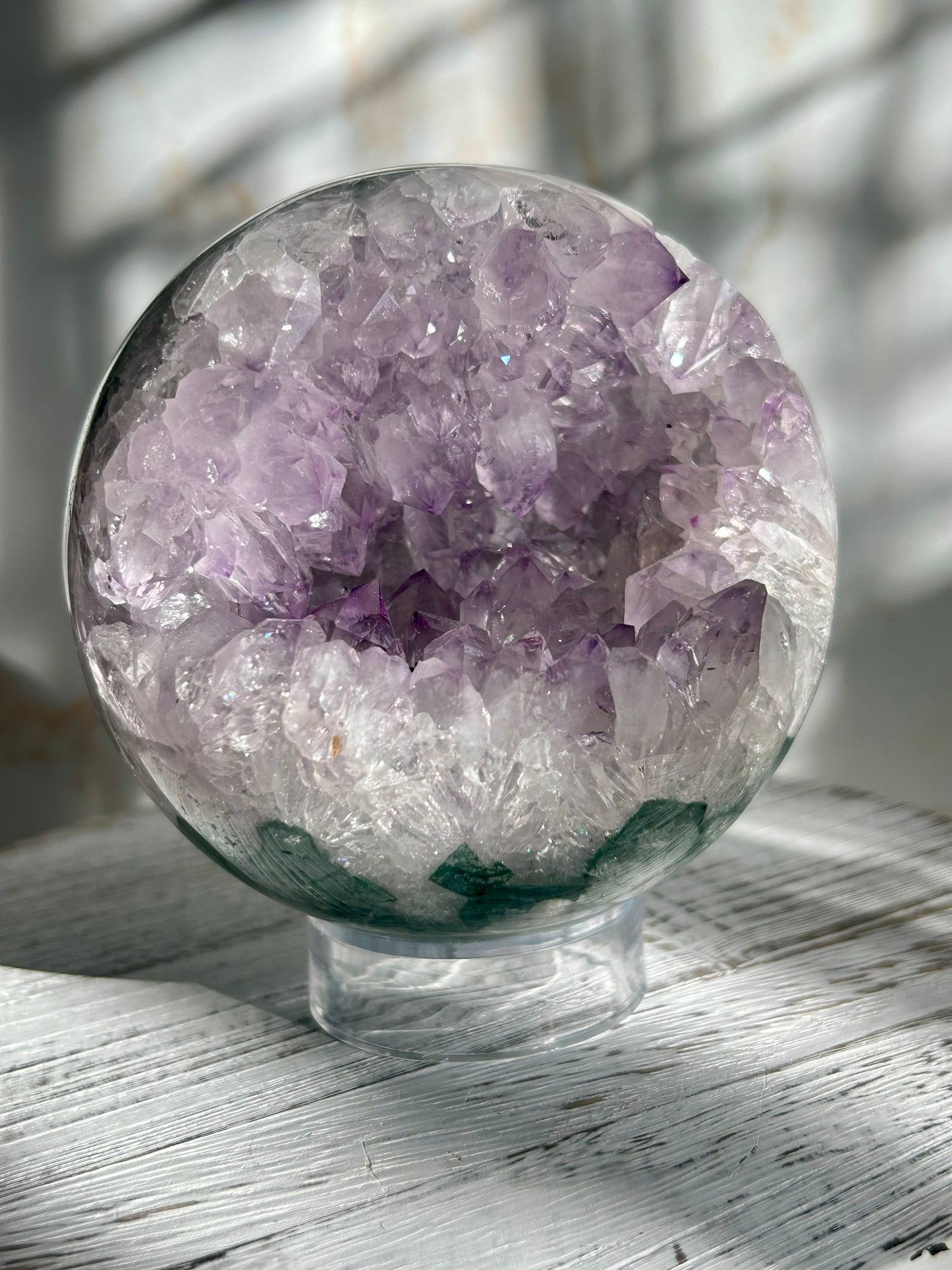 Polished Amethyst sphere with natural green mineral inclusions, glowing lavender points and earthy depth under natural light
