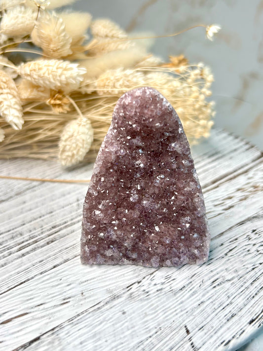 Amethyst cut base from Uruguay with vibrant violet crystal points and polished edges, displayed on a rustic white stand beside dried florals.