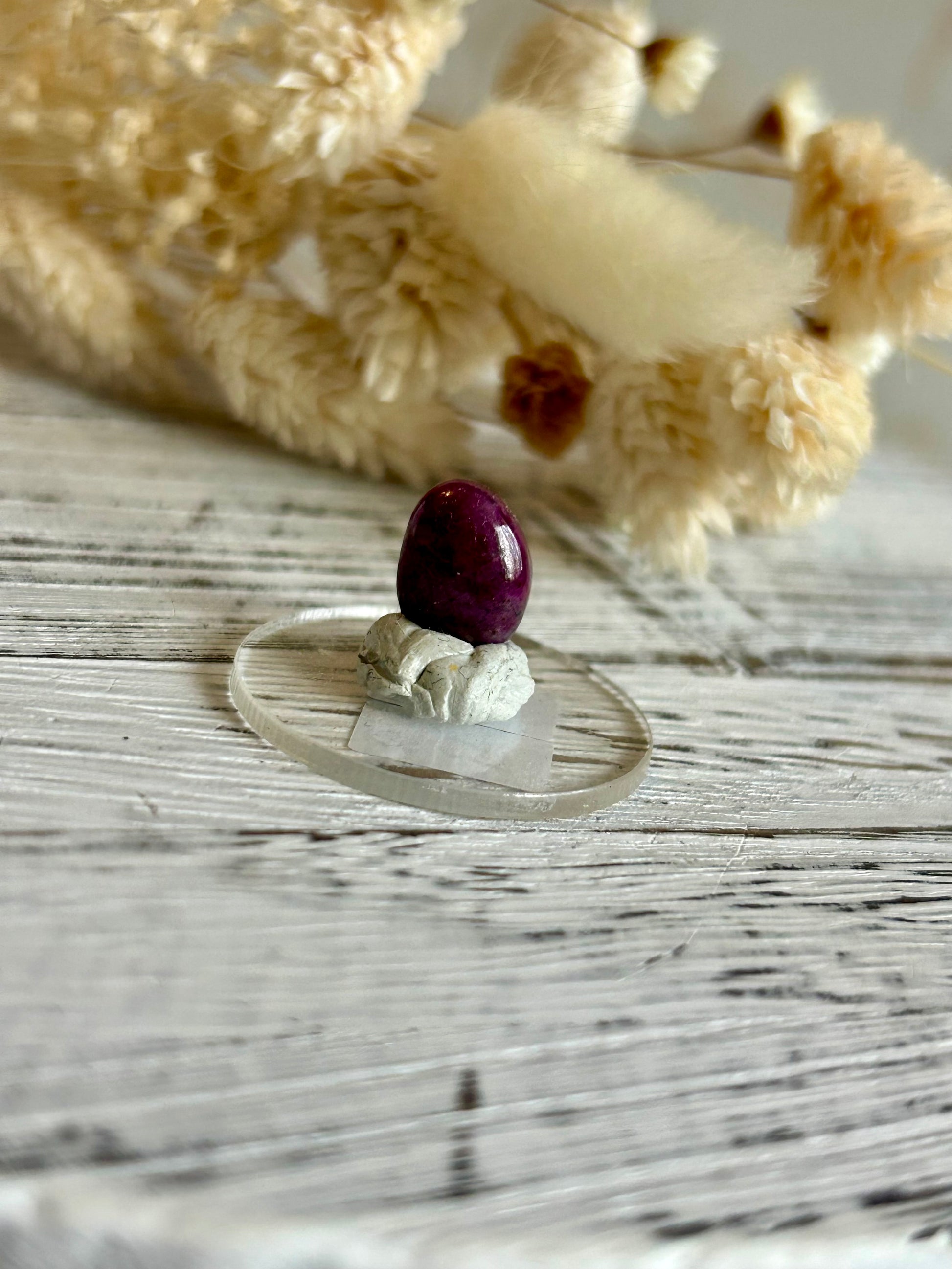 Polished natural Ruby cabochon with deep magenta-red tones, displayed against dried florals in soft natural light