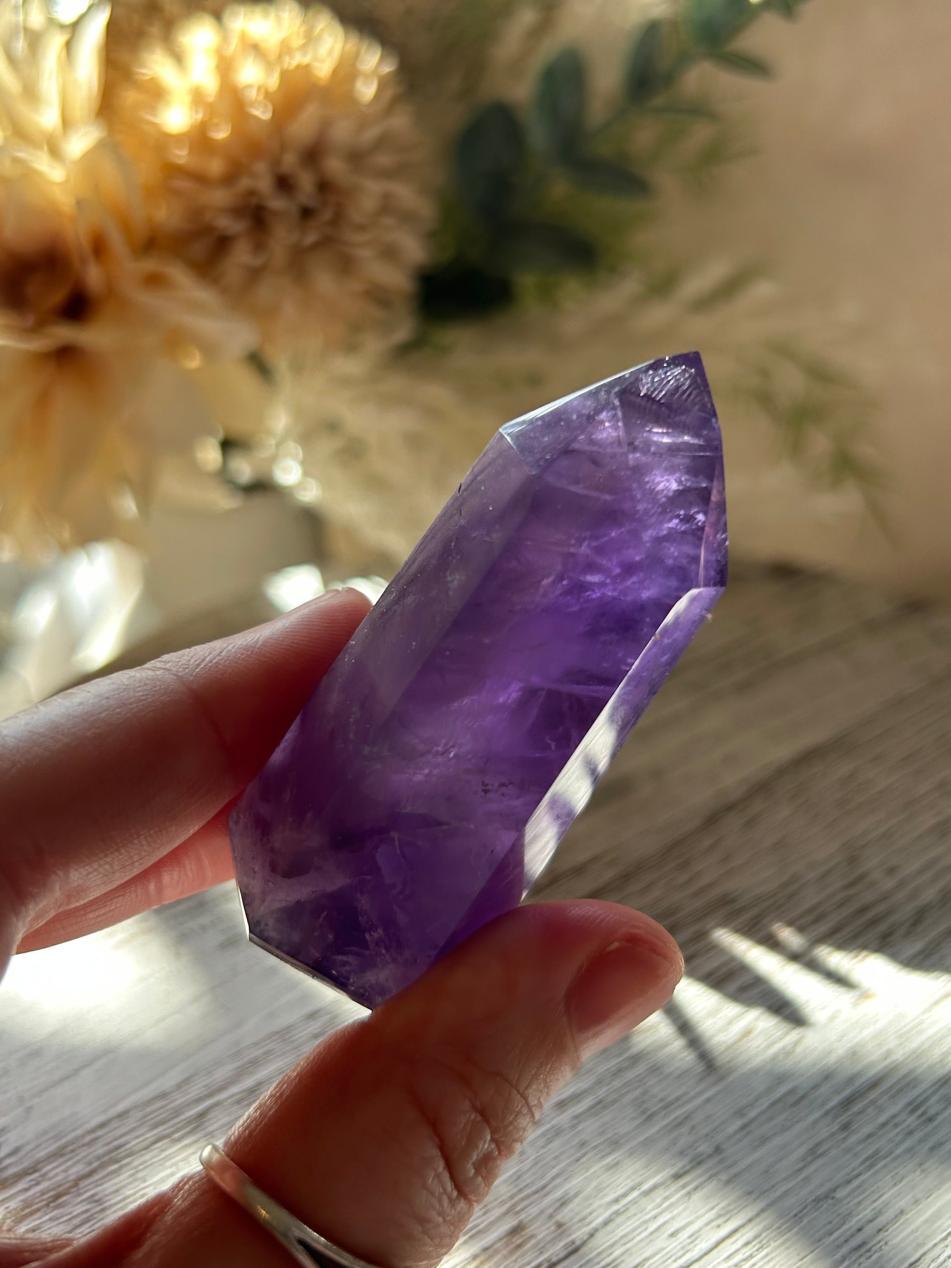 Hand holding a purple crystal with a blurred natural background