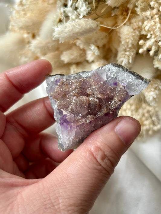 Small druzy rainbow sugar geode clusters with pastel tones and glittering crystal surfaces, displayed on ivory silk with cream dried flowers in the background.