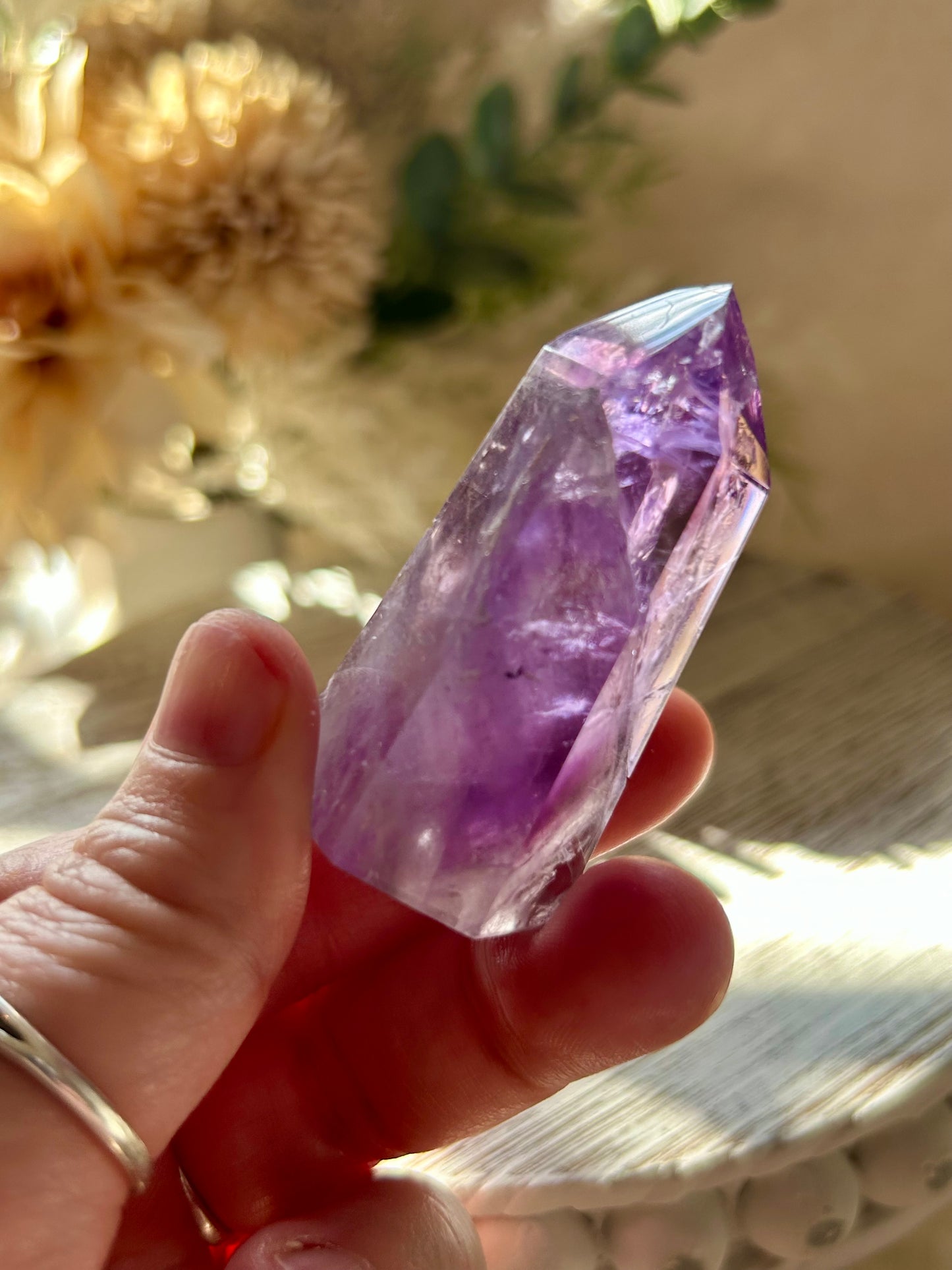 Hand holding a purple crystal with a blurred natural background