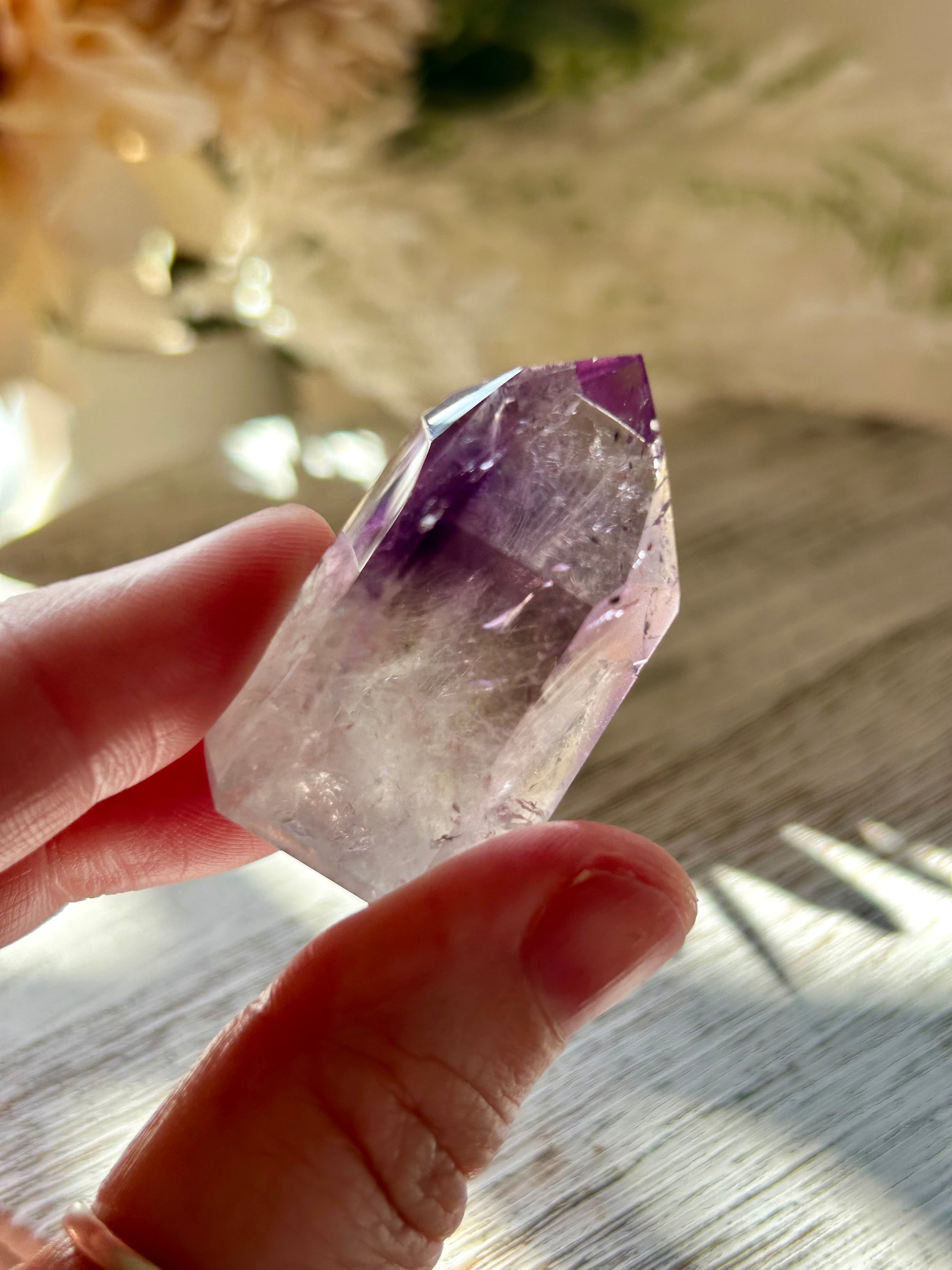Hand holding a clear crystal with purple interior on a wooden surface