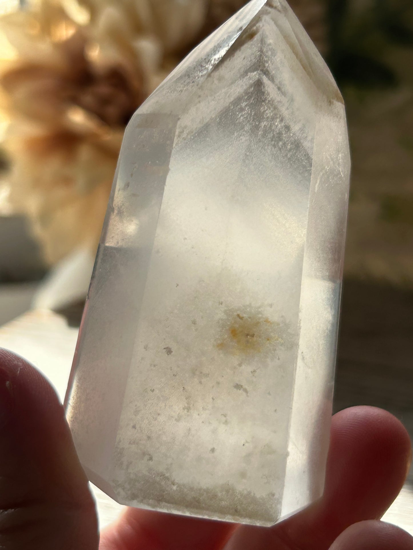 Clear crystal held by a hand with a blurred natural background