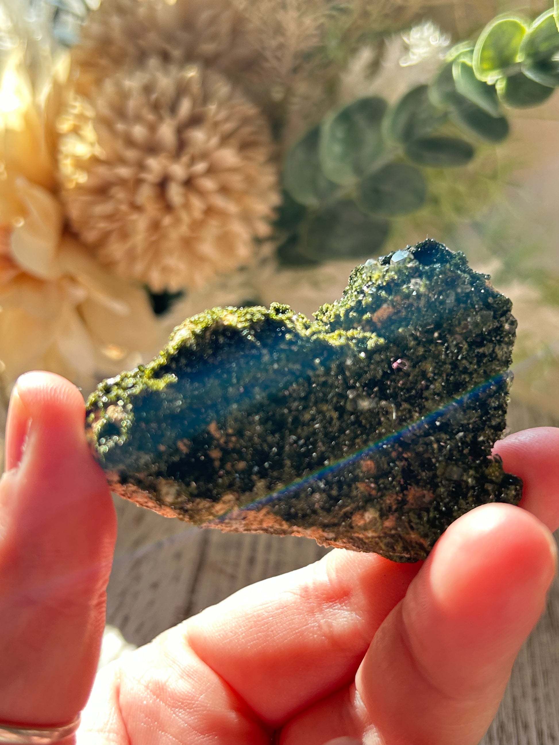 Person holding a dark green mineral or rock with a blurred natural background