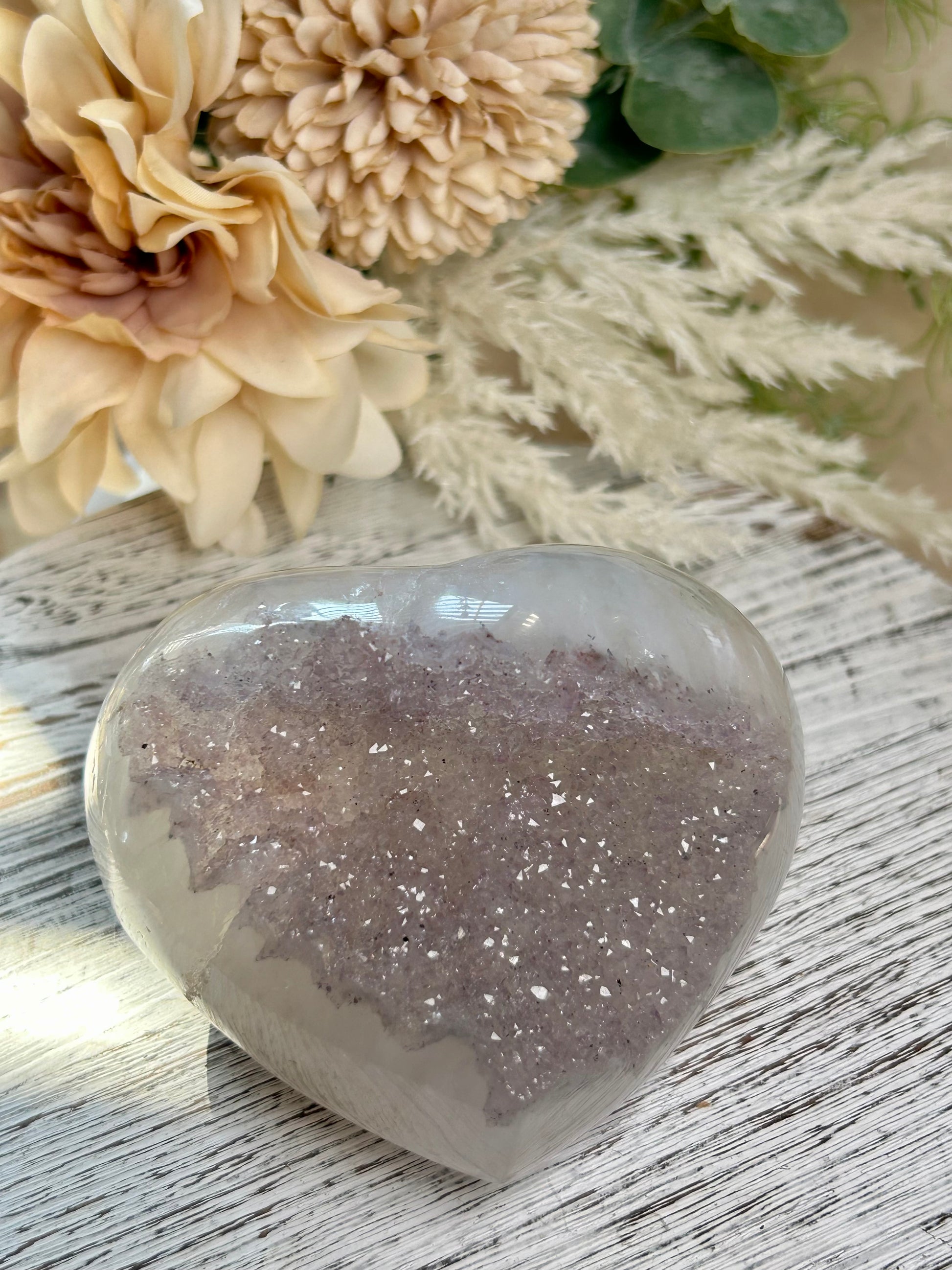Heart-shaped decorative stone with glittery texture on a wooden surface with flowers in the background