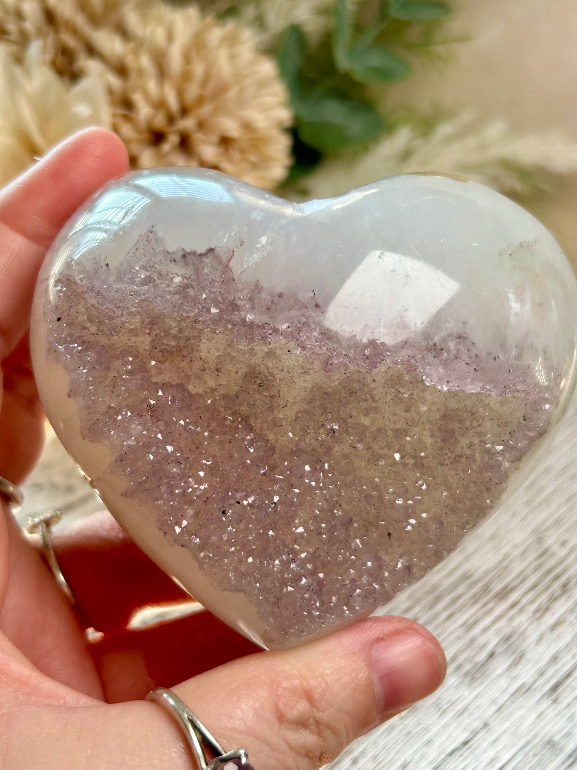 Heart-shaped crystal with glittery interior held by a hand on a wooden surface.