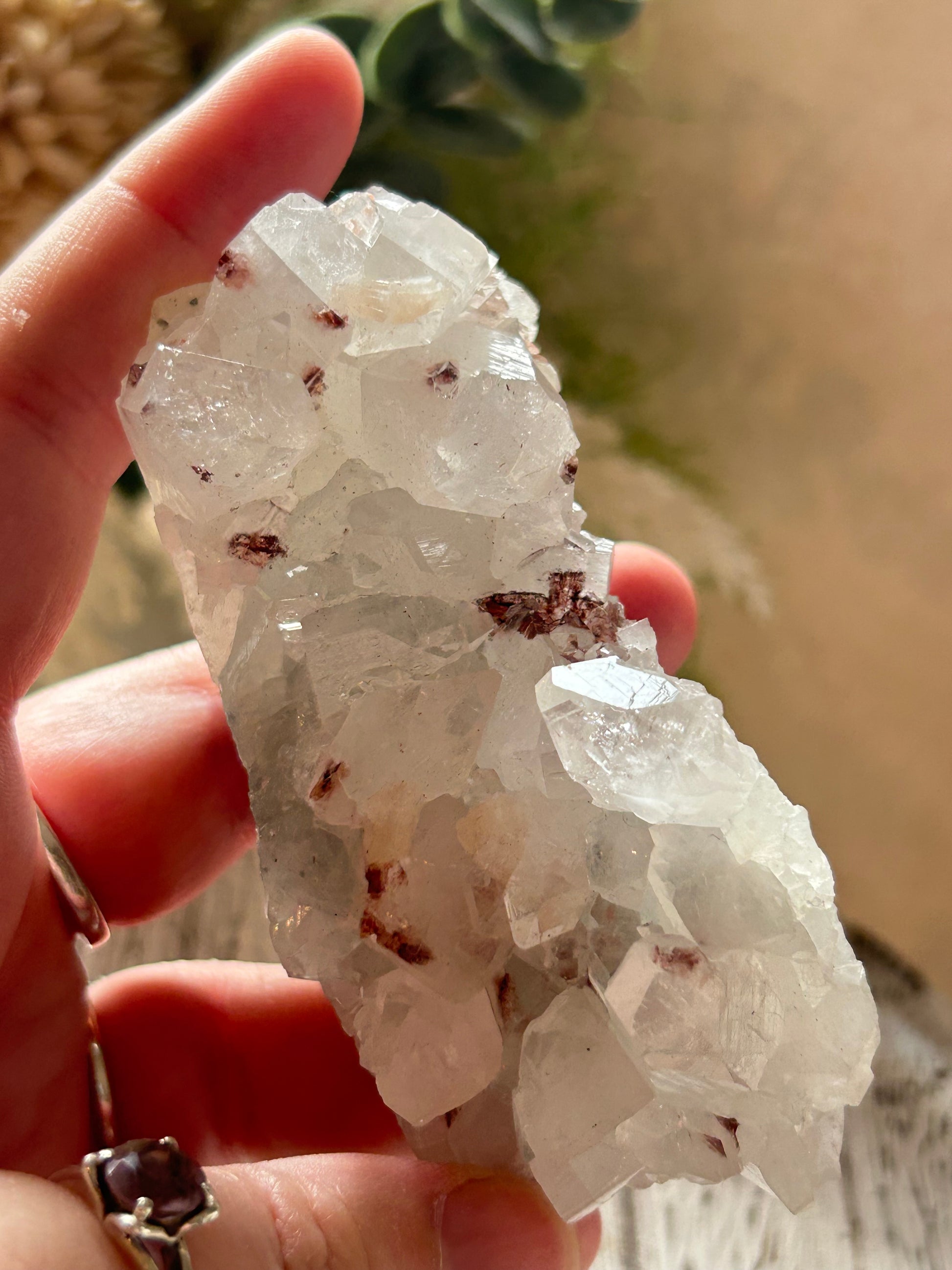 Clear crystal cluster held in a hand with a blurred natural background