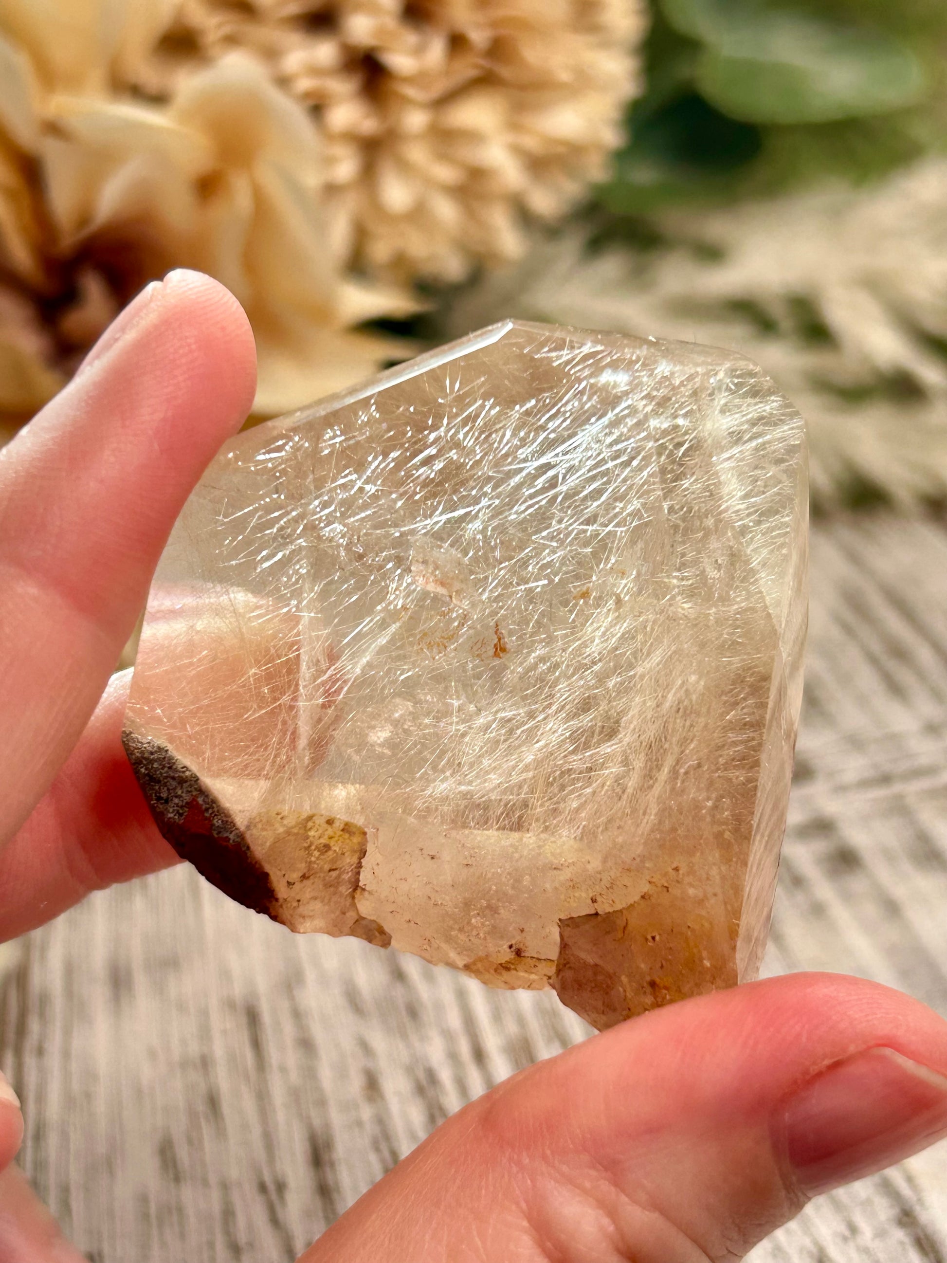 Clear crystal held between fingers with a blurred natural background