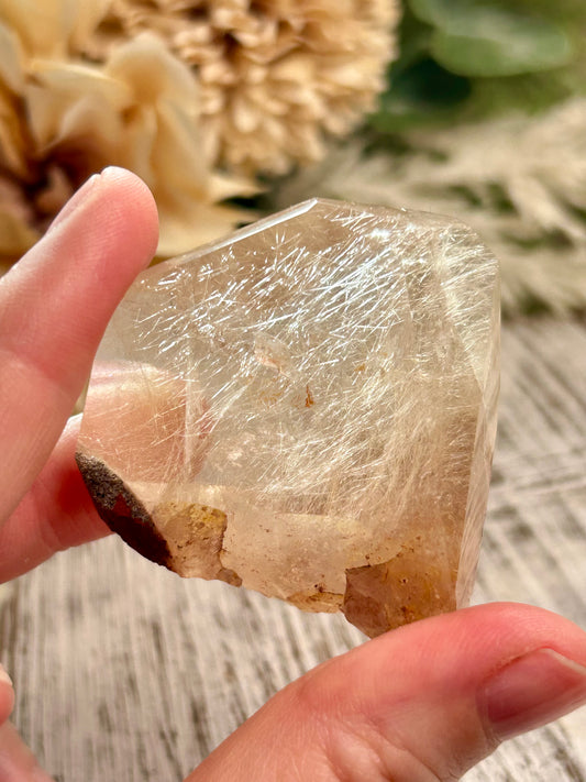 Clear crystal held between fingers with a blurred natural background