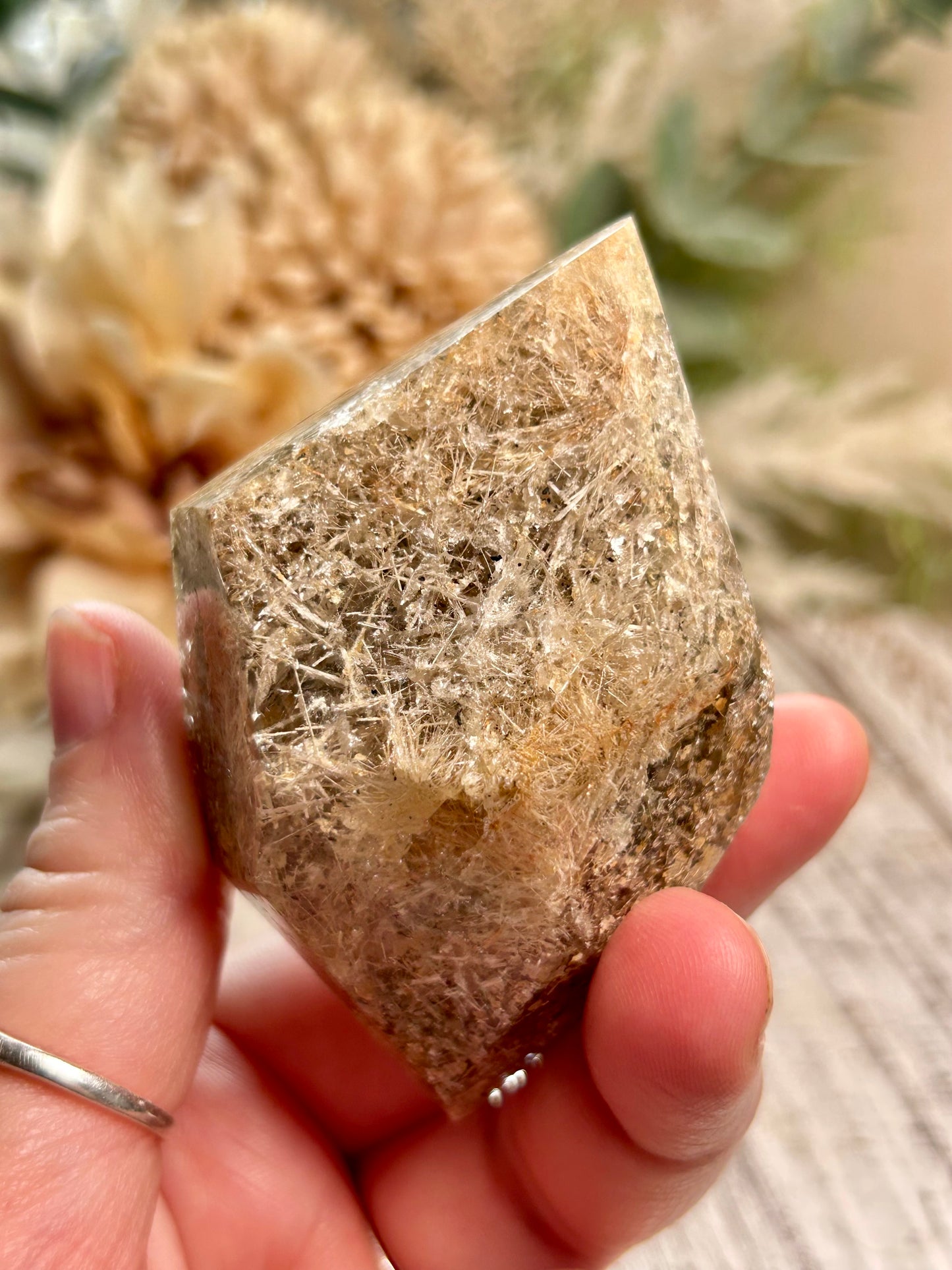 Hand holding a rough-hewn crystal with natural fibers against a blurred outdoor background