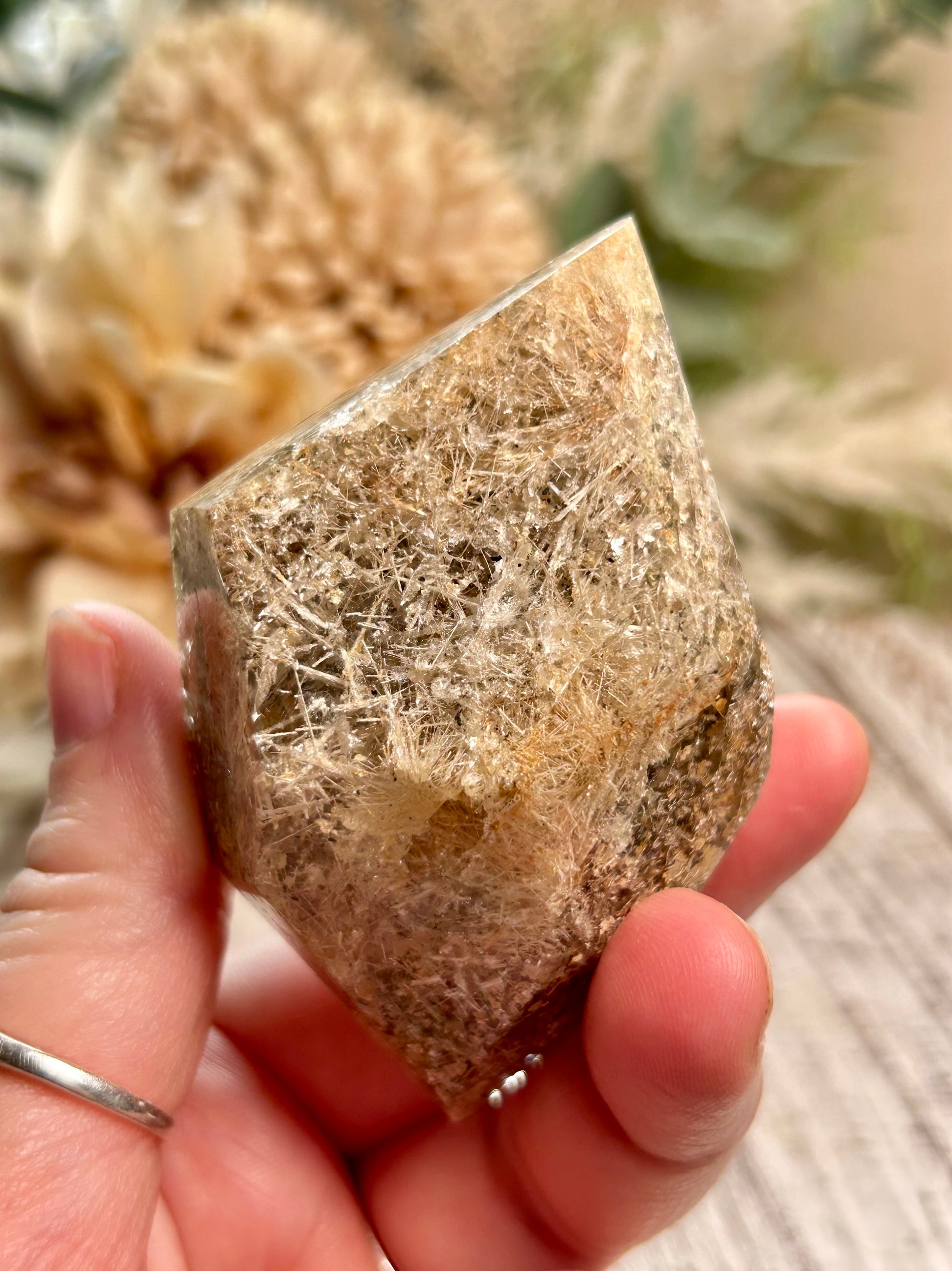 Hand holding a rough-hewn crystal with natural fibers against a blurred outdoor background