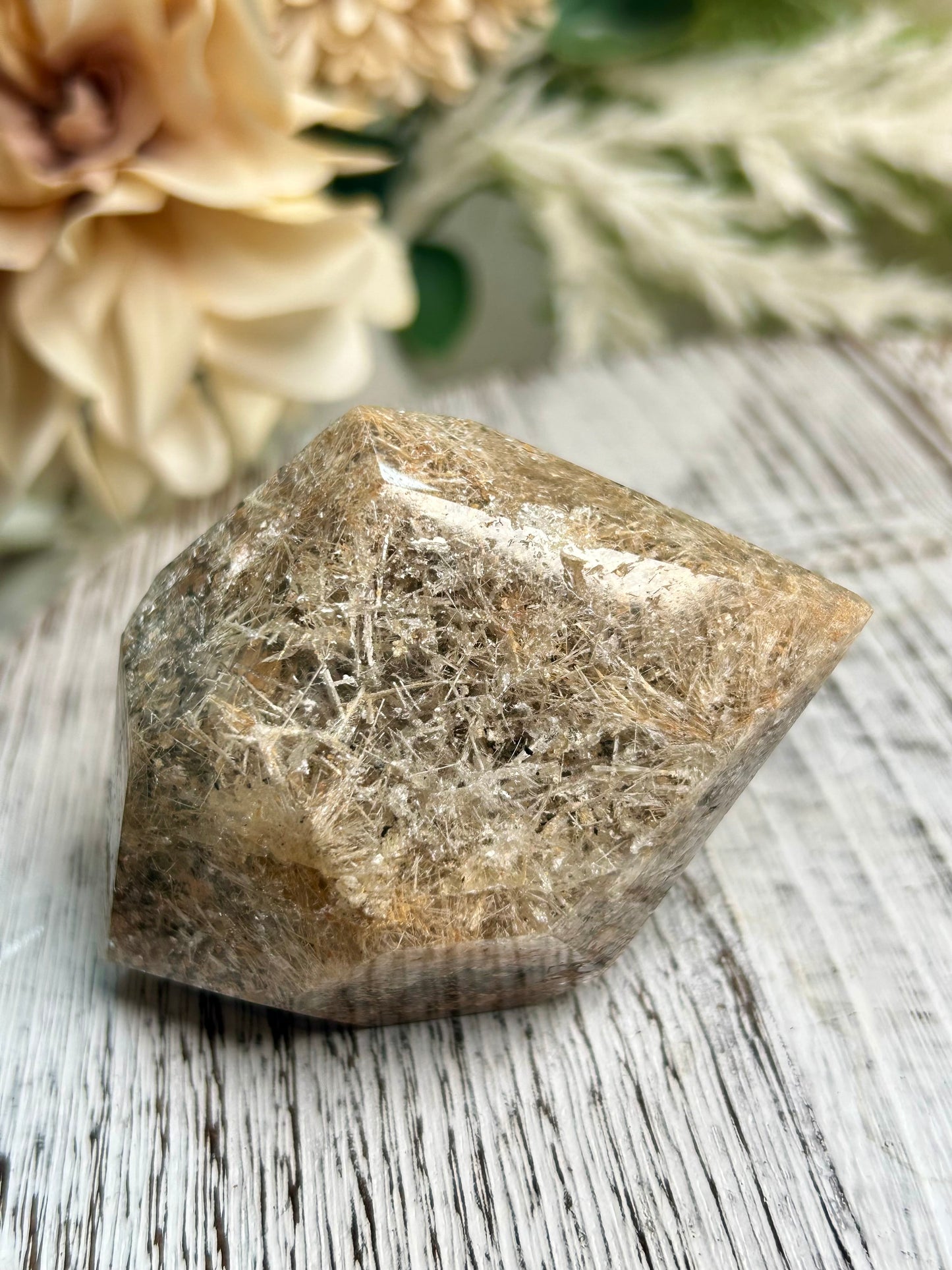 Raw crystal rock on a wooden surface with flowers in the background
