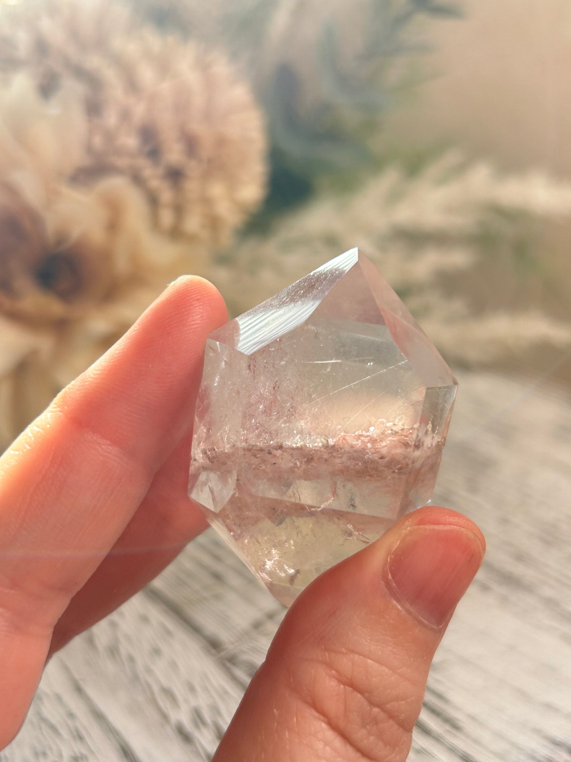 Hand holding a clear crystal with a blurred natural background