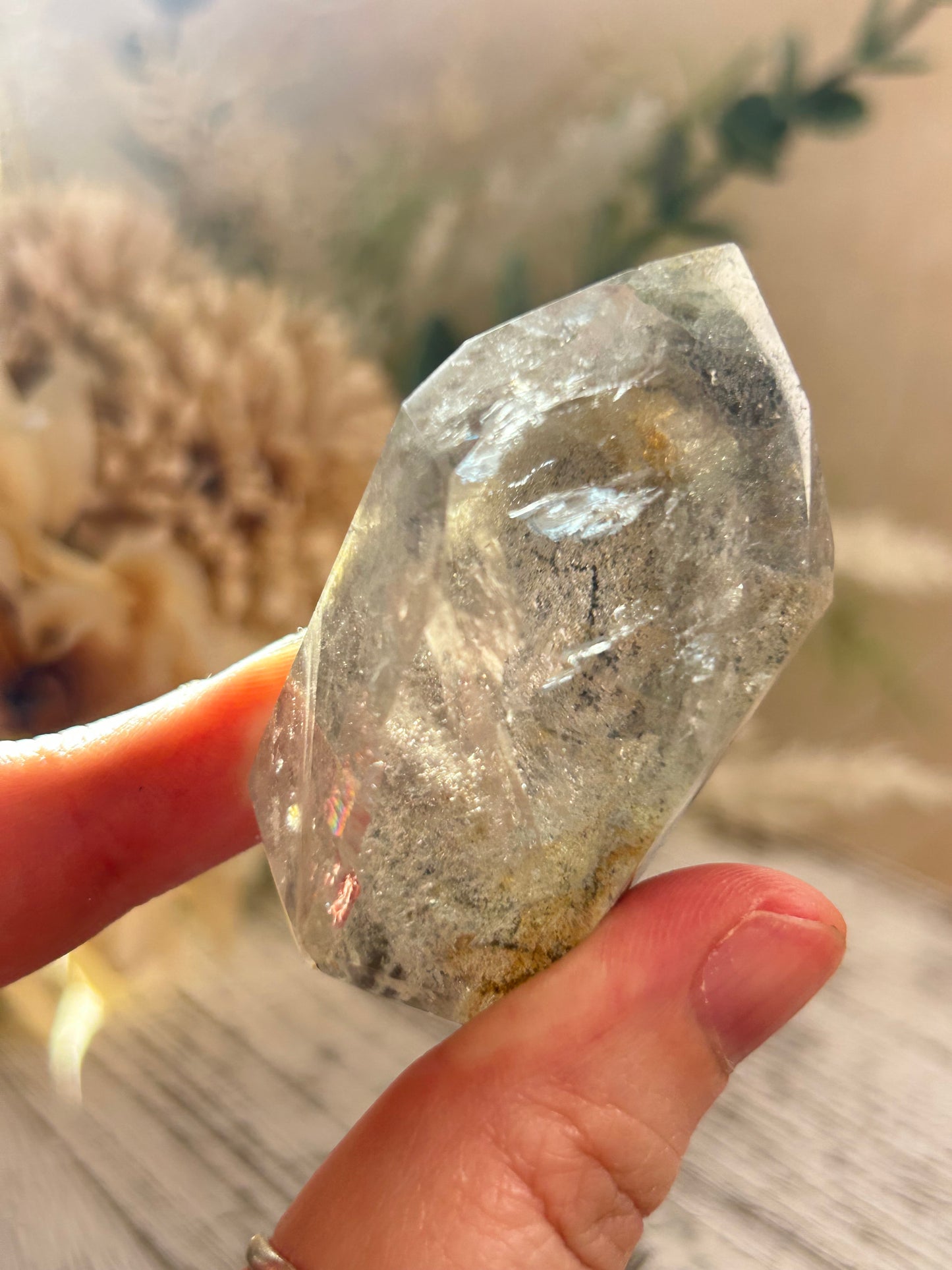 Clear crystal held between fingers with a blurred natural background